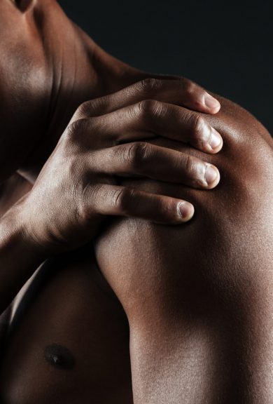 Cropped photo of young shirtless afro american man with shoulder pain, isolated on black background